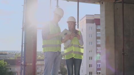 business-building-teamwork-technology-and-people-concept---smiling-builders-in-hardhats-with-tablet-pc-computer-outdoors